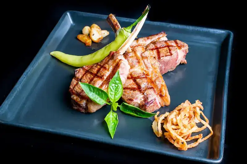 Grilled lamb chops with a green chili, basil and crispy onions on a dark square plate