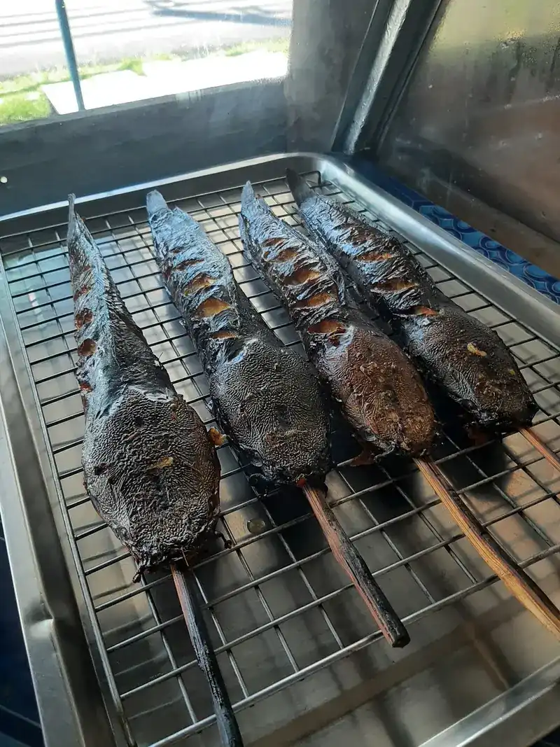 Four whole fish grilled on bamboo skewers on a steel tray