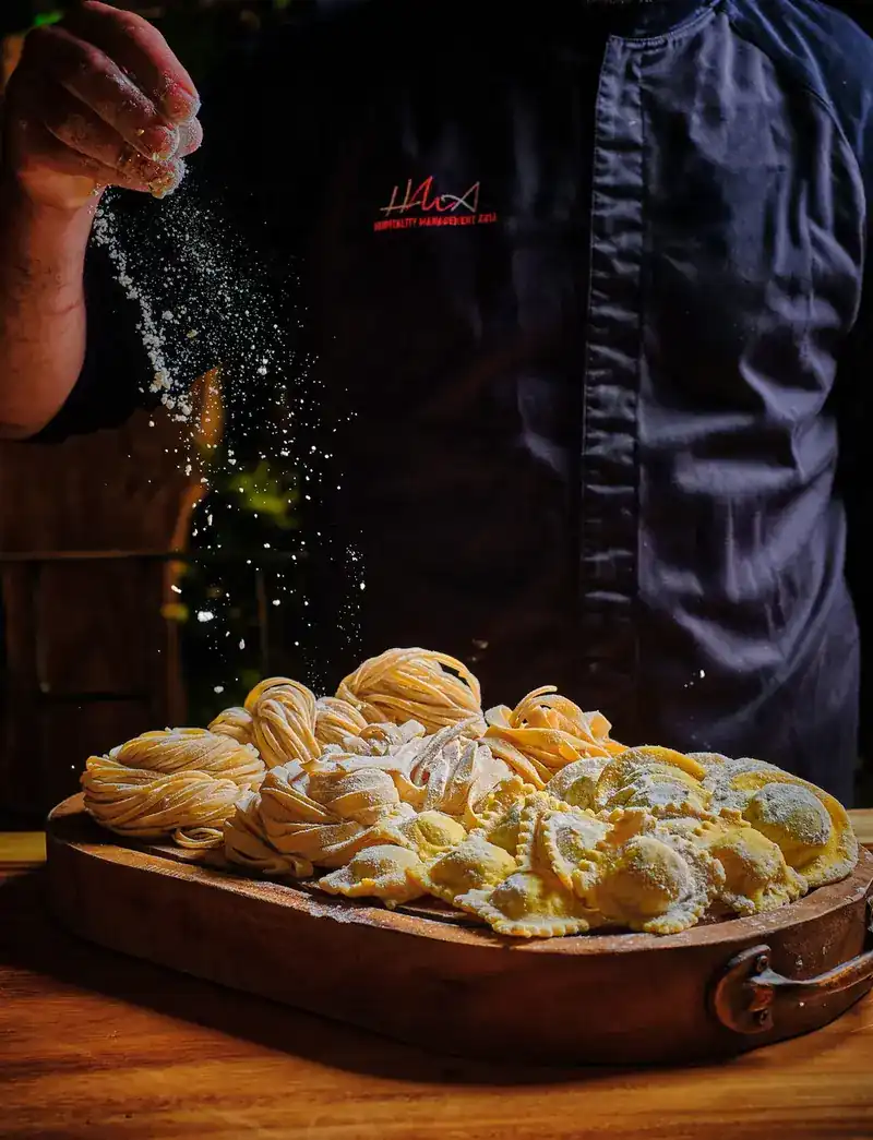 Flour dusted over nests of fresh pasta and ravioli on a wooden board