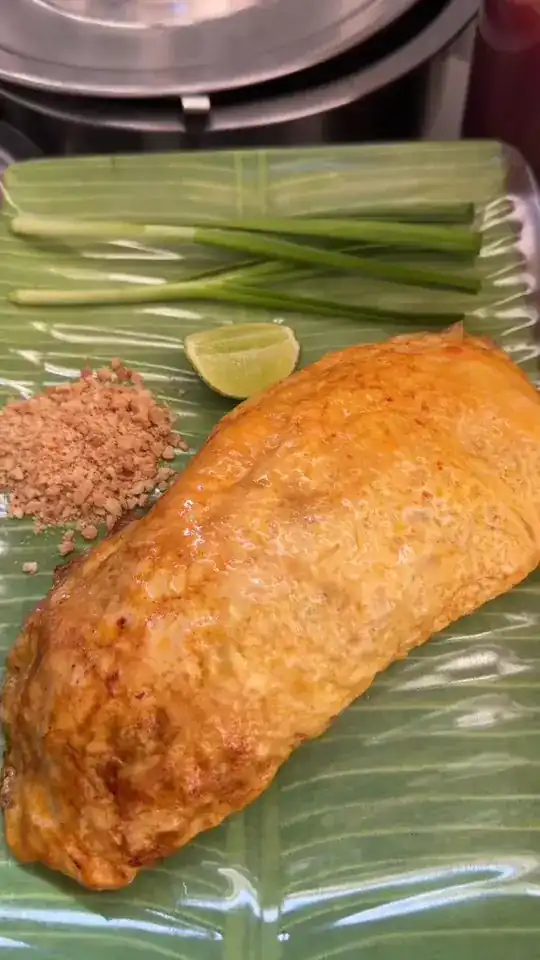 Pad thai wrapped in a golden omelette on a banana leaf, with spring onion, lime and ground peanuts