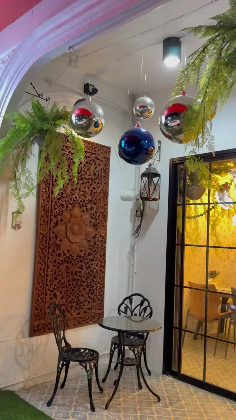 The entrance: a carved wooden panel, an iron bistro table with two chairs and mirrored balls under the awning