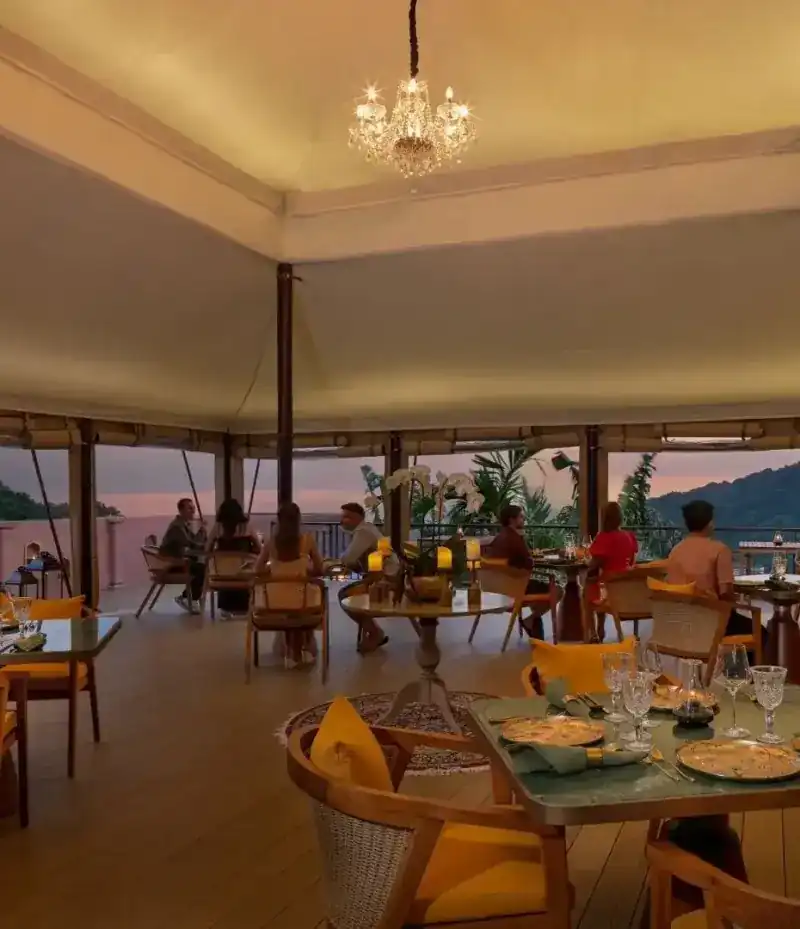 Inside the tent at sunset: canvas ceiling, a chandelier, tables along the open side facing the sea