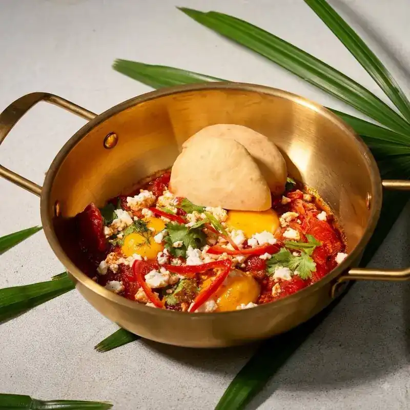 Shakshuka with eggs, peppers and feta in a brass pan, with bread