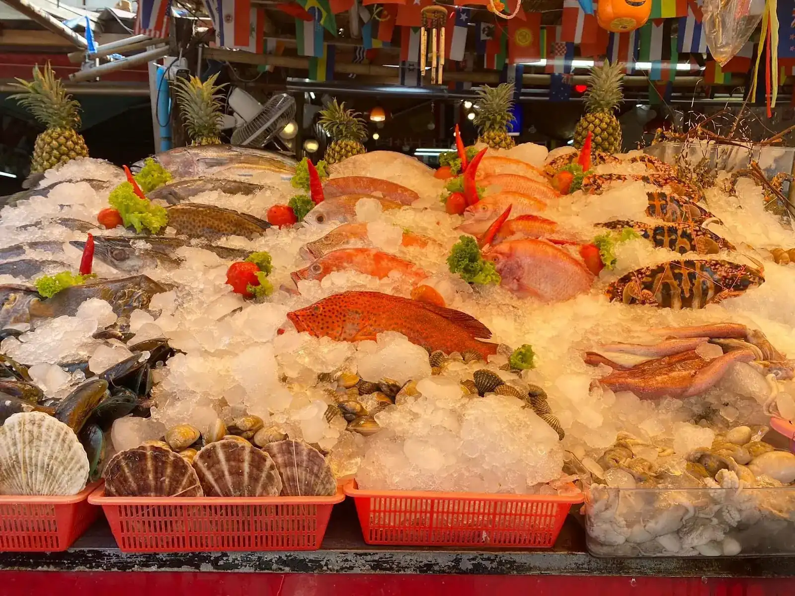 Fish, crabs, scallops, clams and squid laid out on crushed ice at the front of Bounty Seafood, with pineapples behind