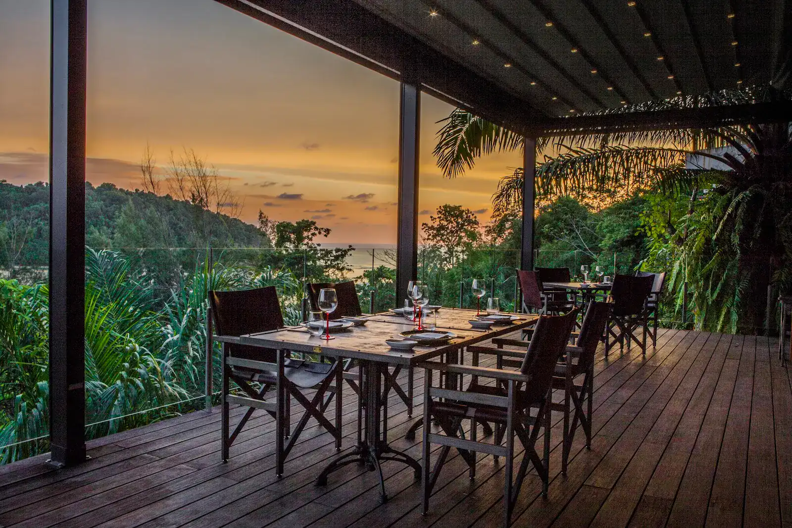Terrace tables at sunset above the trees, the sea in the distance / โต๊ะบนระเบียงยามพระอาทิตย์ตก เหนือยอดไม้ มองเห็นทะเลไกล ๆ