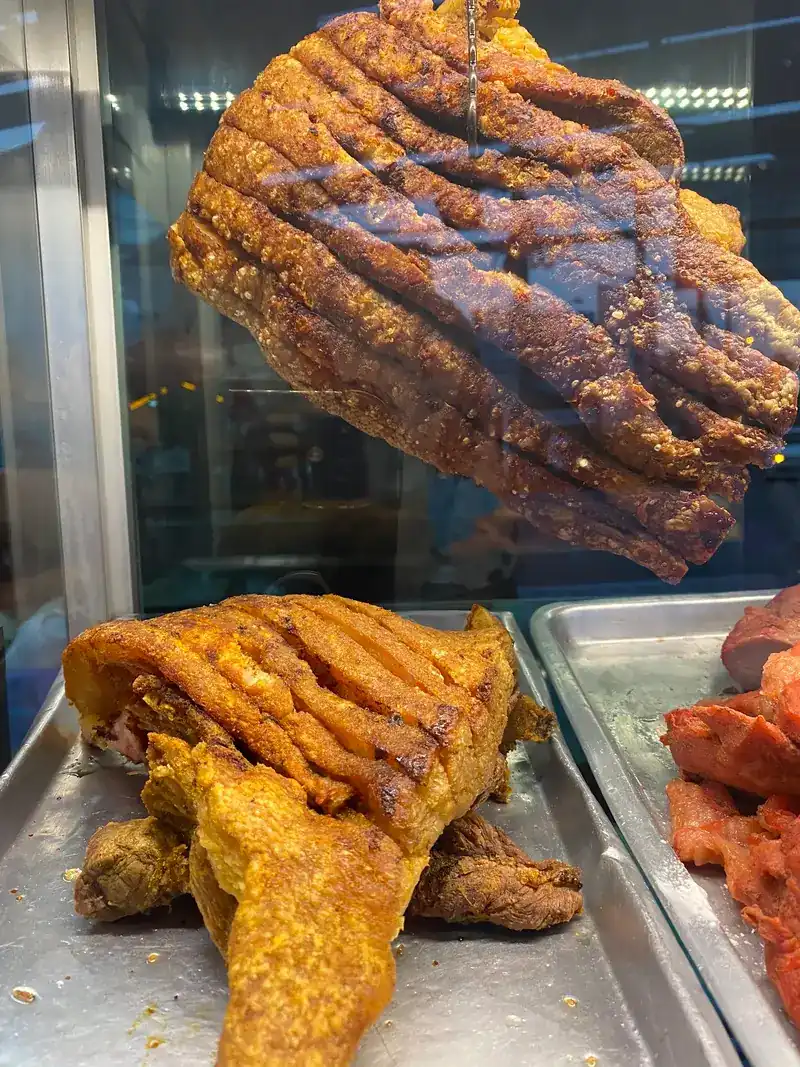 Crispy pork hanging in the glass case, with red pork on the tray beside it
