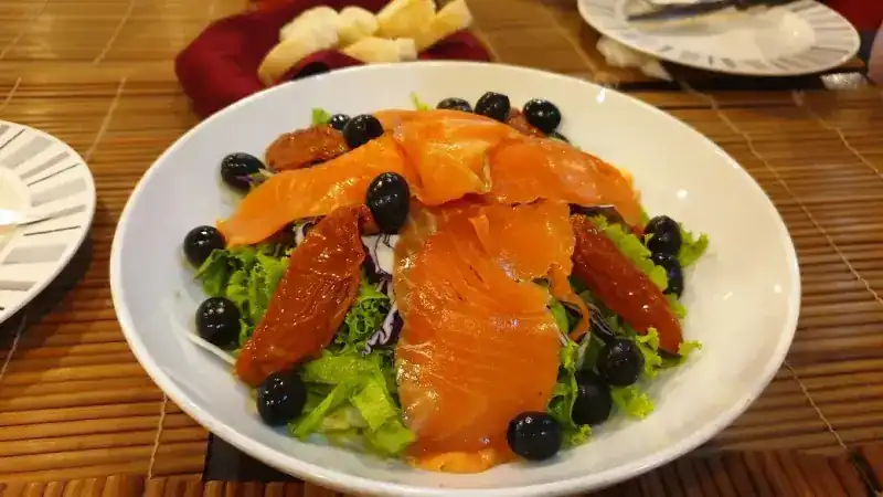 Smoked salmon salad with black olives and sundried tomato in a white bowl