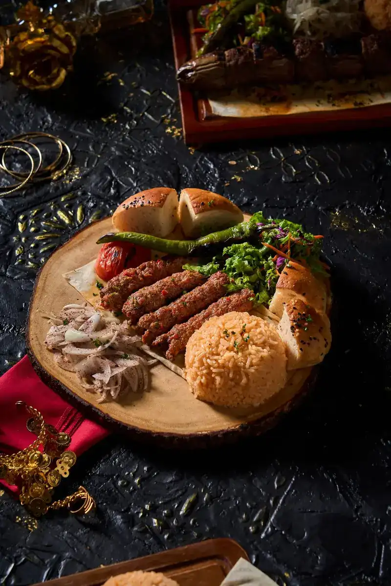 Grilled kebabs on a round wooden board with bread, peppers, rice and onions