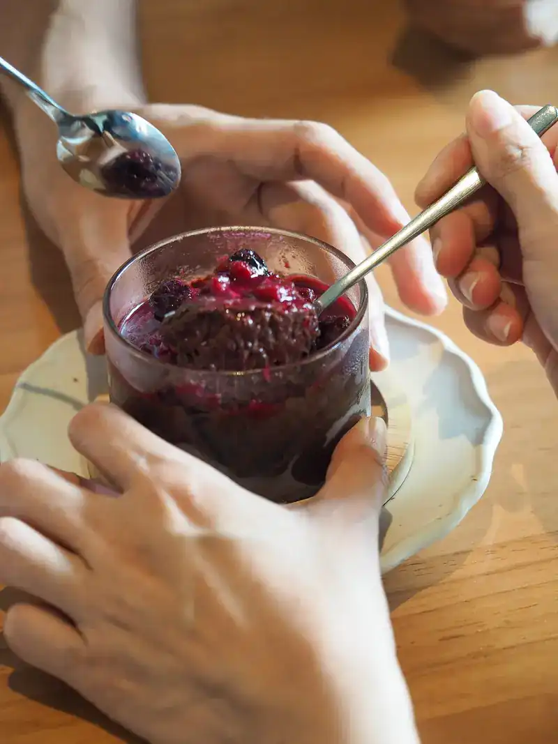 Two spoons sharing a dark dessert with berries in a glass