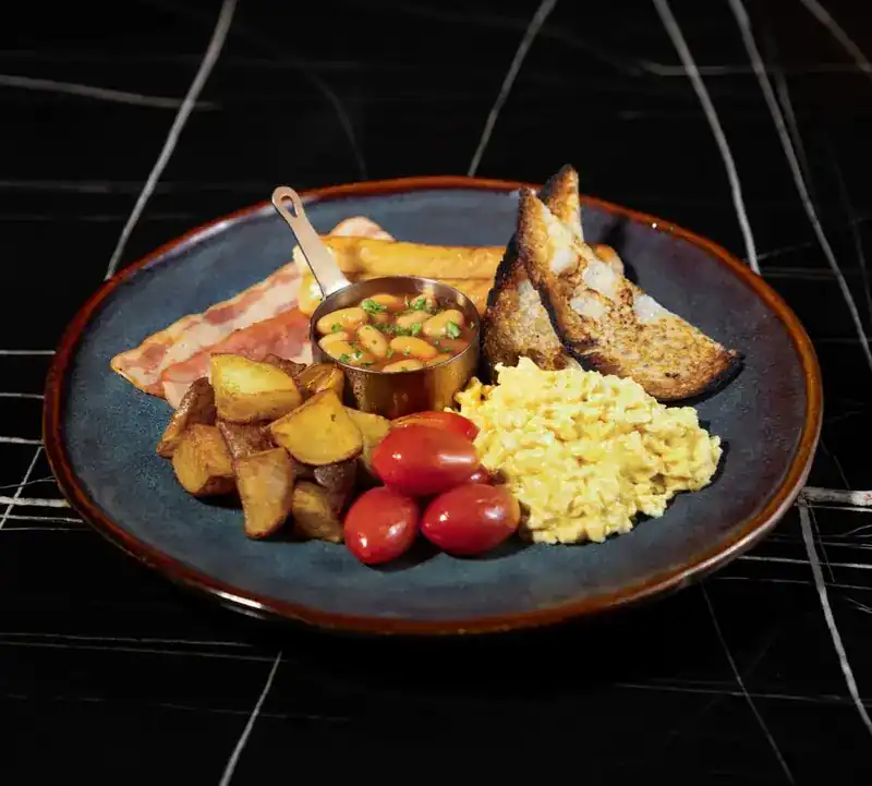 English breakfast on a blue plate: scrambled eggs, beans, fried potatoes, cherry tomatoes and sourdough