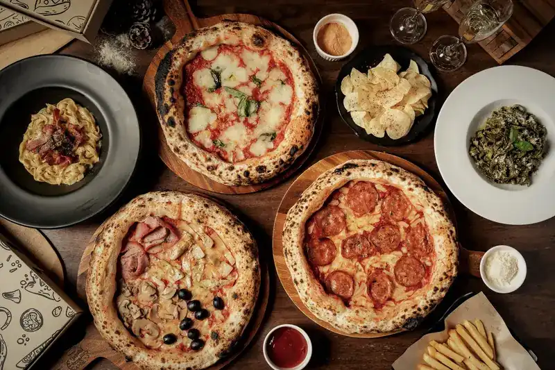 A wooden table from above with three pizzas, pasta and small plates