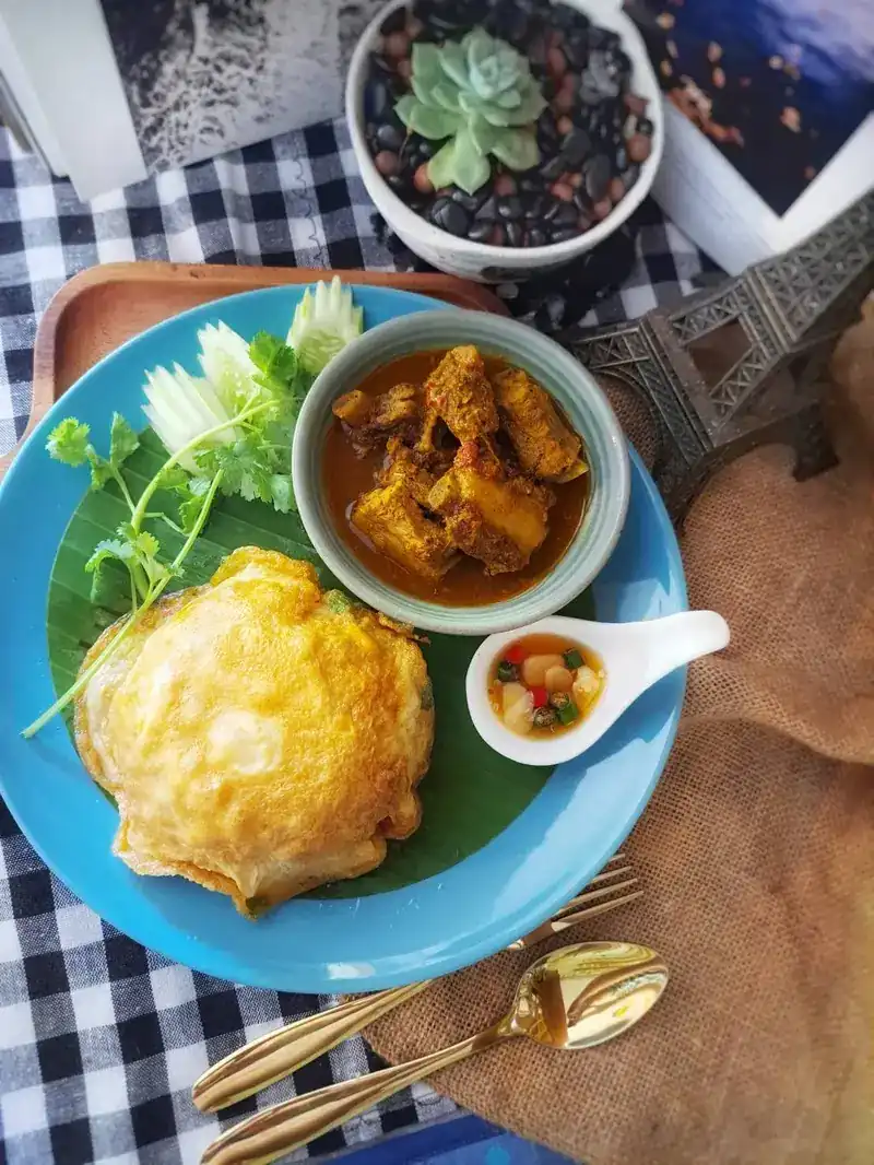 Pork spare-rib curry in a bowl, with an egg, herbs and cucumber on a banana leaf