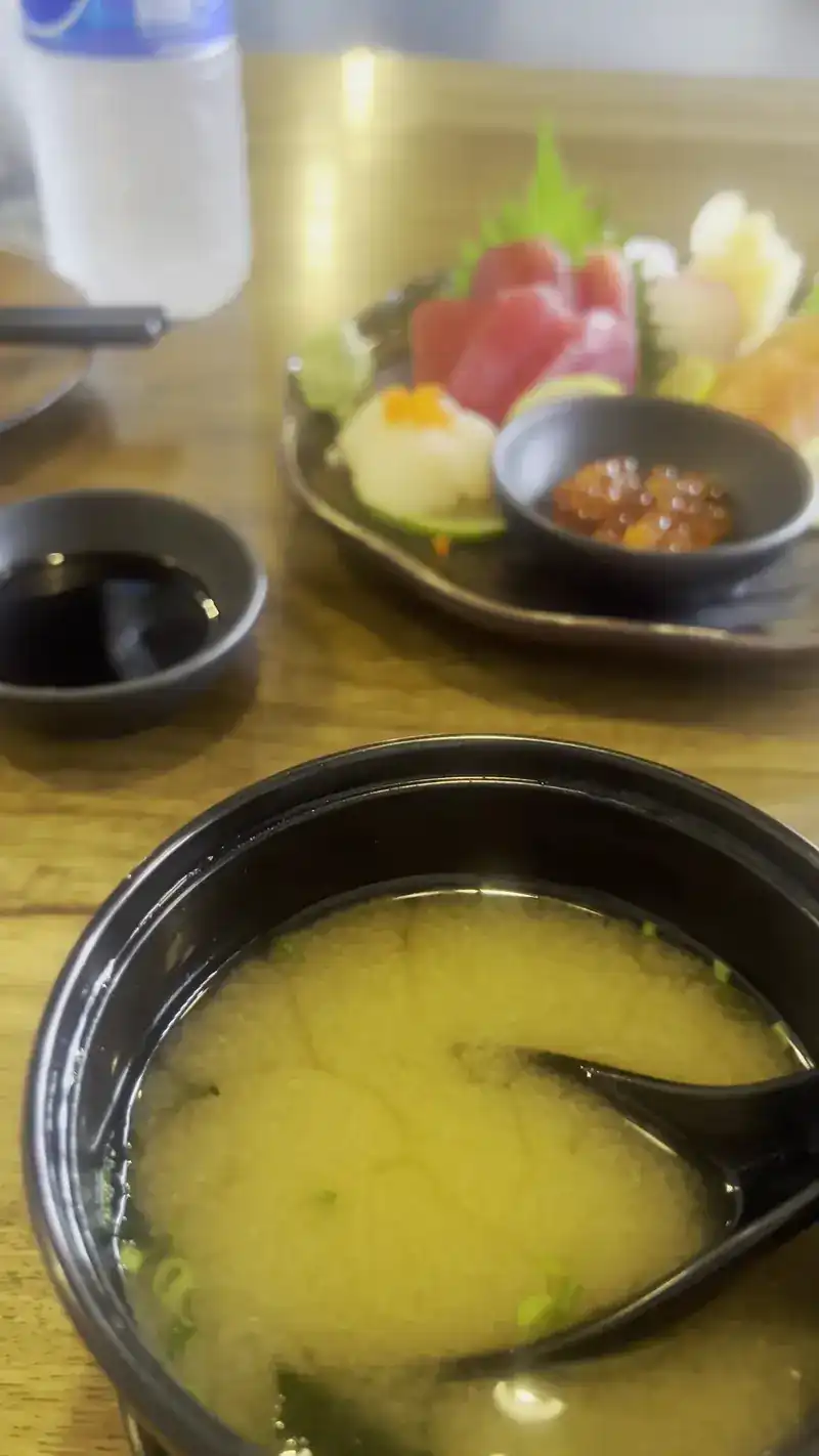 Miso soup in a black bowl, with a sashimi plate behind it
