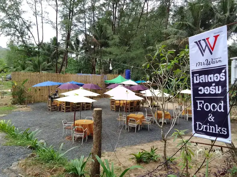 The garden: parasols over wooden tables on gravel, a bamboo fence and the Mr.Warm banner