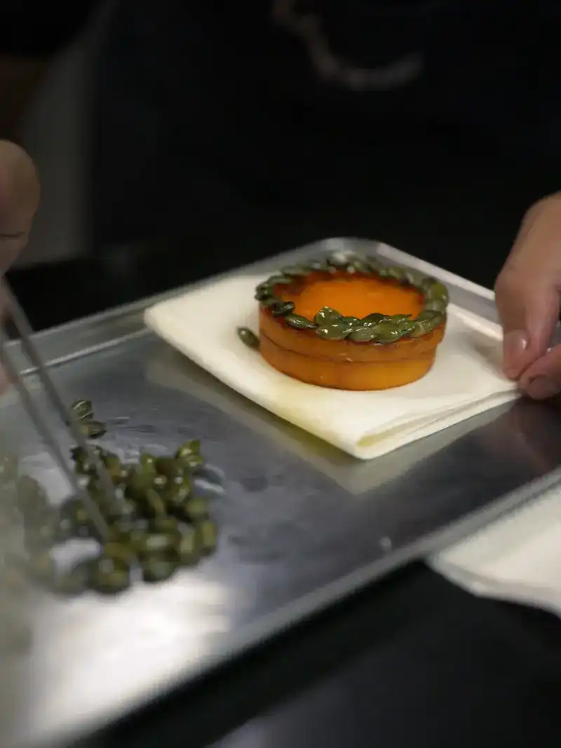 In the kitchen, a small tart being finished with tweezers on a steel tray
