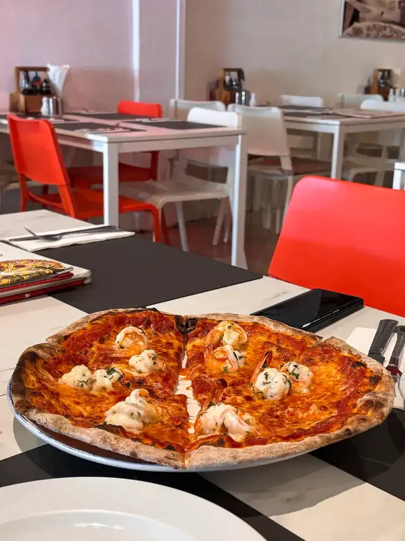 A seafood pizza on a table in the dining room, red chairs behind