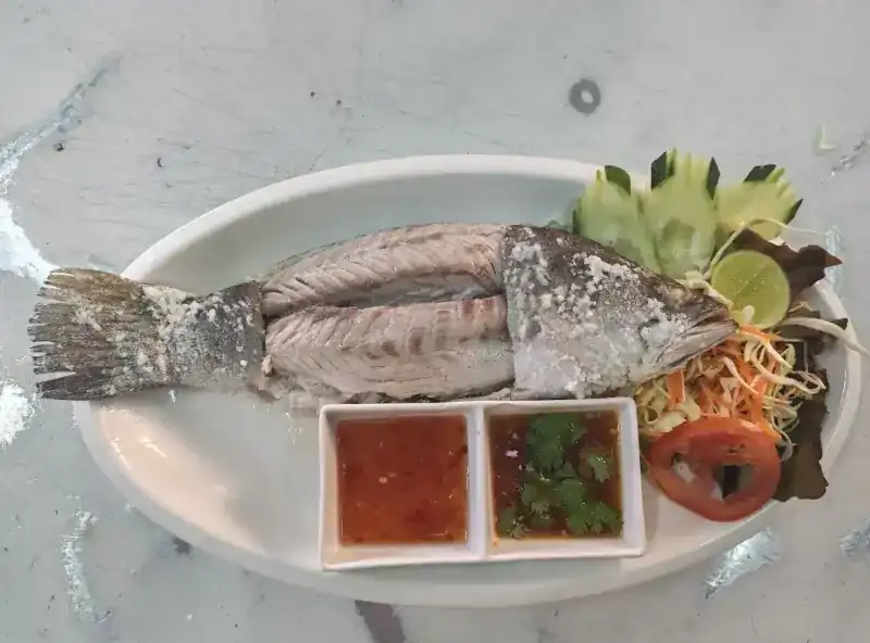 A whole fish grilled in a salt crust, with two dipping sauces, lime and salad