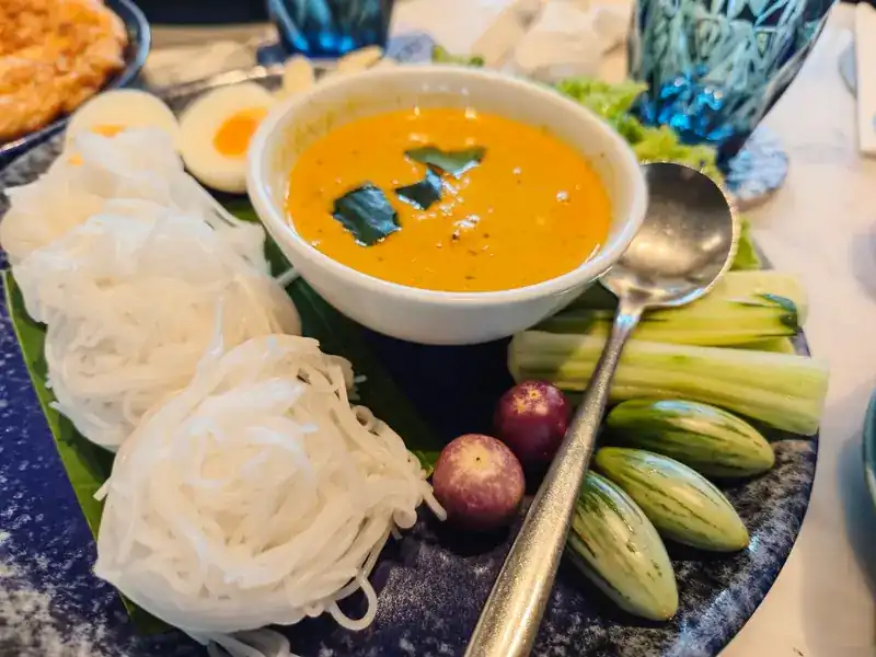 Rice noodles with an orange curry, boiled eggs, cucumber and small Thai eggplants