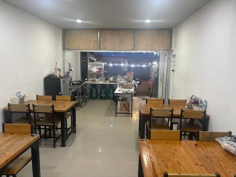 Inside the shop: wooden tables along white walls and the noodle counter at the open front