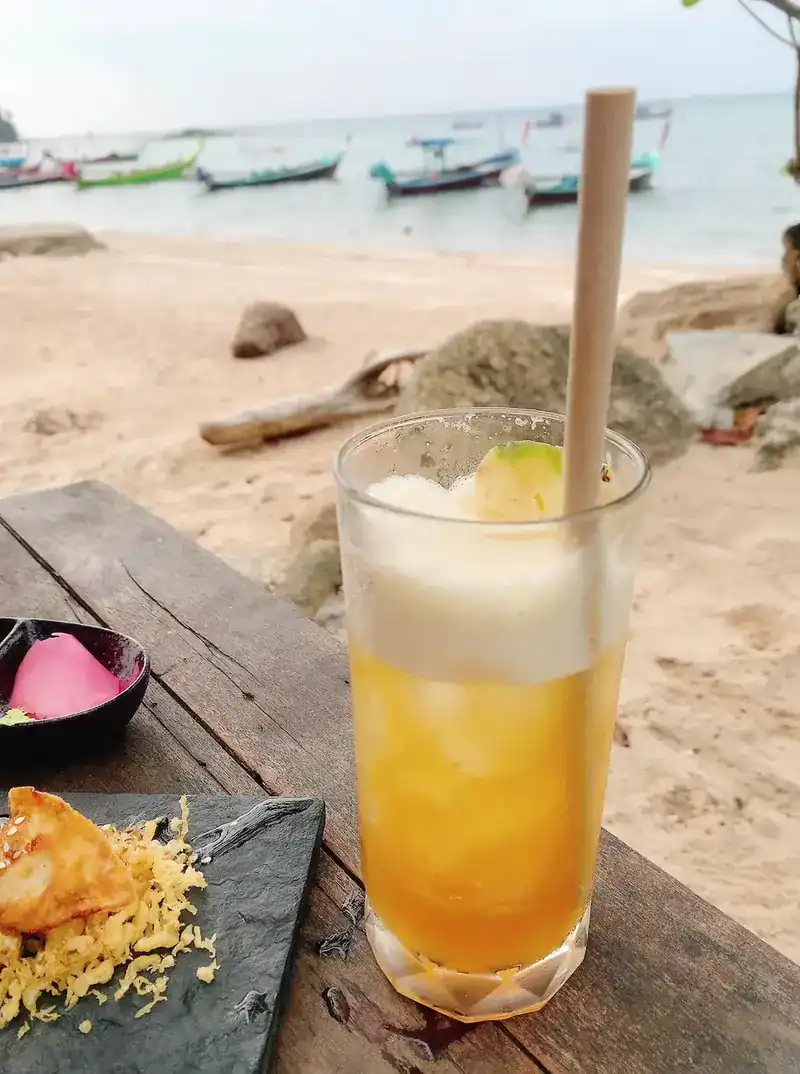 A cold drink with a paper straw on a wooden table above the beach