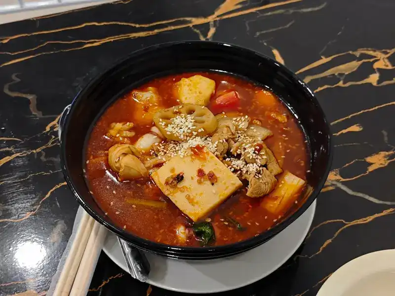Red mala soup with tofu and lotus root in a black bowl
