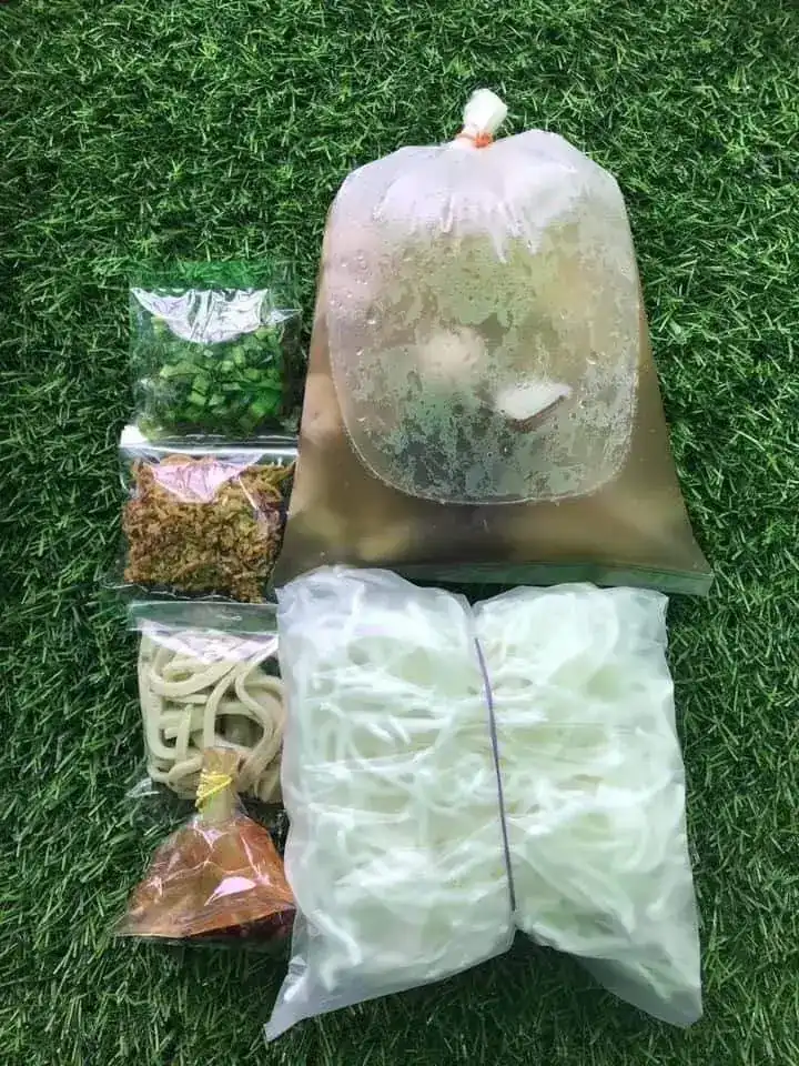 A take-home pack on green turf: soup with pork balls in a bag, rice noodles, herbs and fried garlic packed apart