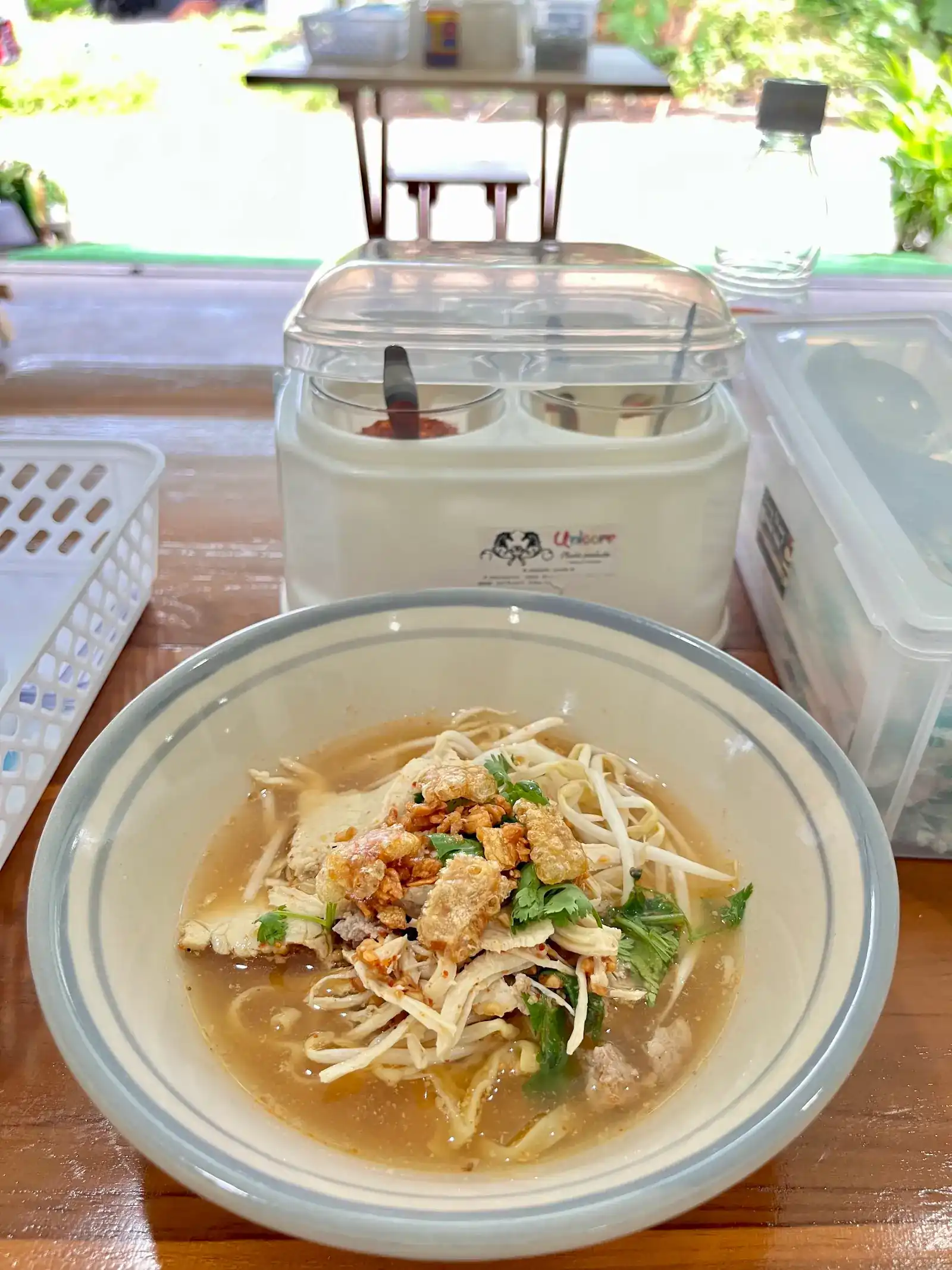 A bowl of tom yum noodles with chicken, minced pork, bean sprouts and coriander, the condiment caddy behind it