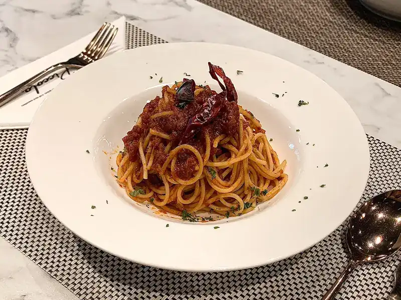 A plate of spaghetti in red sauce topped with whole dried chillies, on a marble table