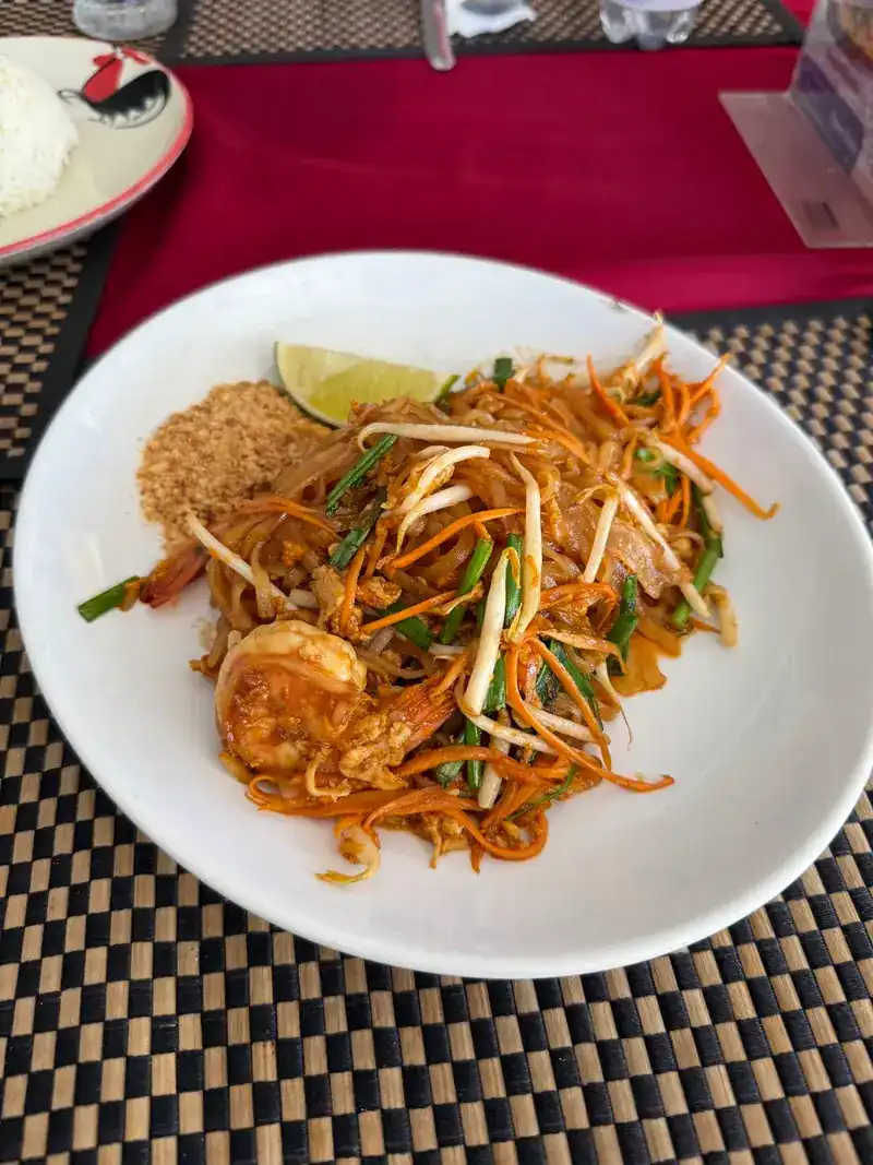 Pad thai with prawns, a wedge of lime and crushed peanuts on a woven placemat