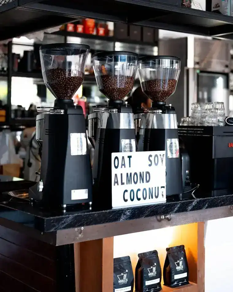 Three grinders full of beans on the coffee bar with a sign for oat, soy, almond and coconut milk