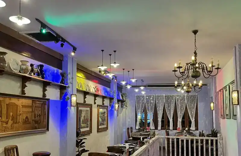 The dining room with a brass chandelier, pendant lamps, framed paintings and lace curtains