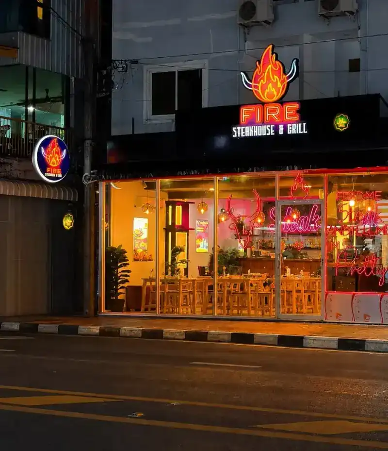 The shopfront at night under its neon flame sign