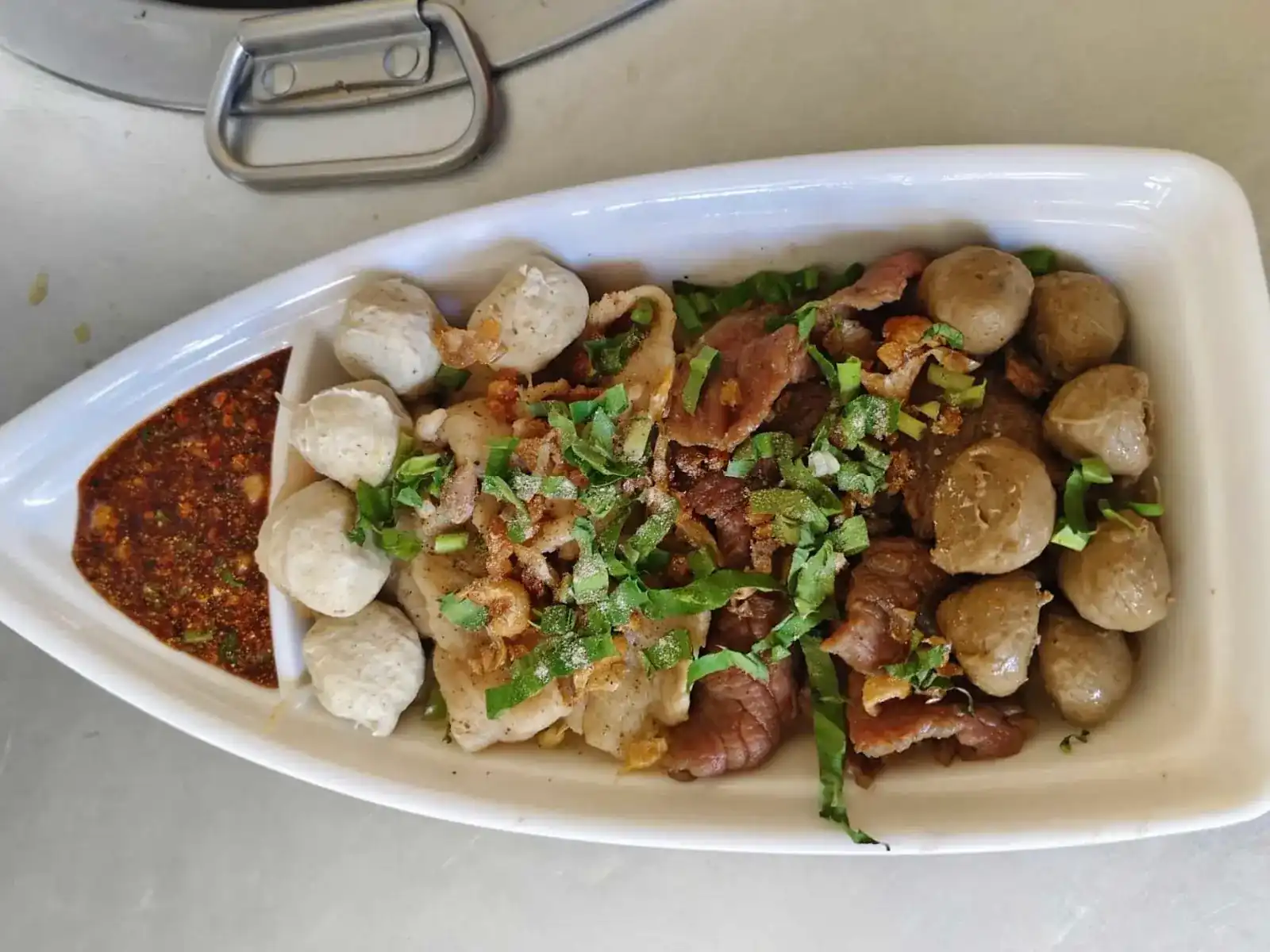 Sliced meat and meatballs in a boat-shaped dish, with a chilli dip