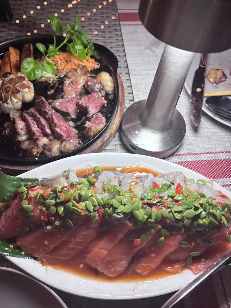 Sliced steak on a hot plate beside a dish of sliced salmon in a spicy dressing