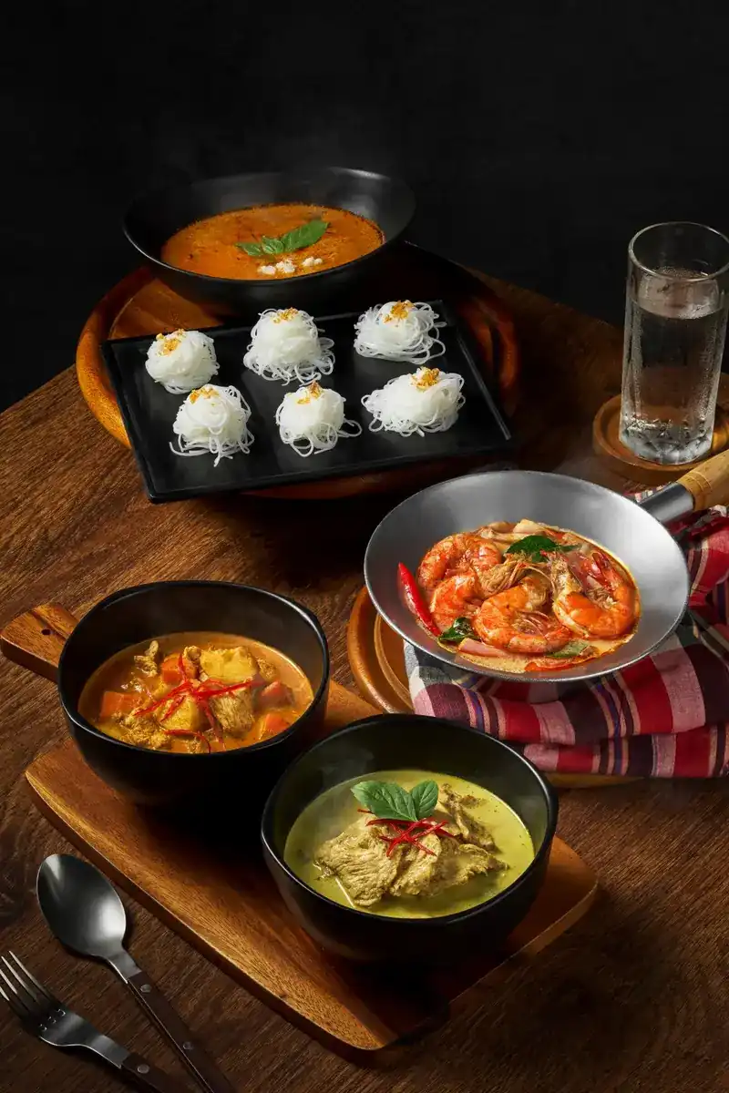 Thai curries, prawns in a pan and nests of rice noodles on a wooden table