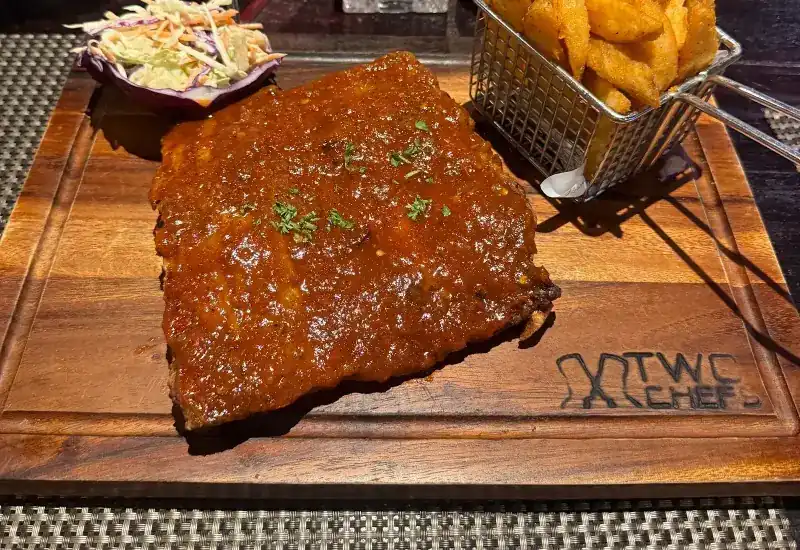 A rack of glazed ribs with fries and coleslaw