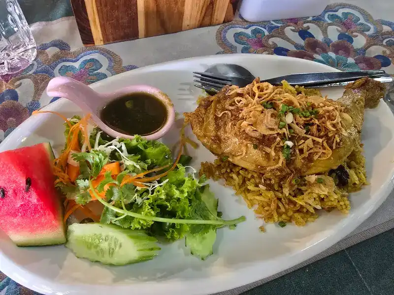 Chicken khao mok: yellow rice with a chicken leg and fried shallots, salad, cucumber and watermelon