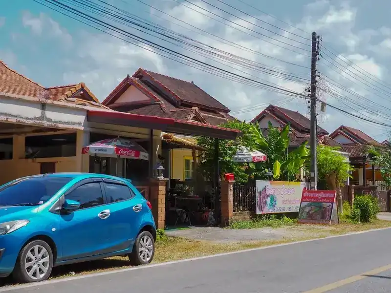 The shop from the road: a house porch with tables behind a brick and iron fence, banana plants, red and white umbrellas and the two shop signs