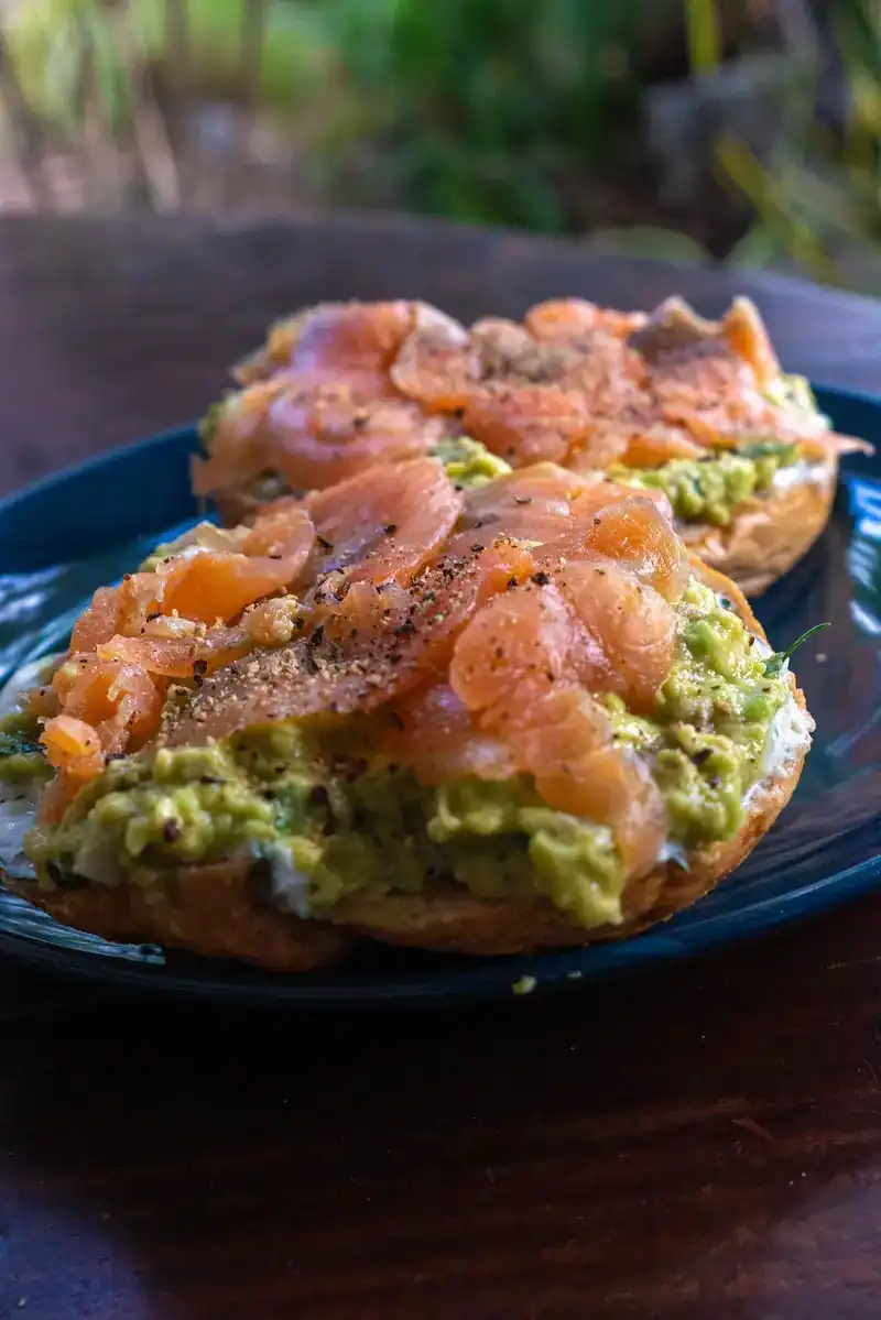 Open bagel halves topped with avocado and salmon and black pepper