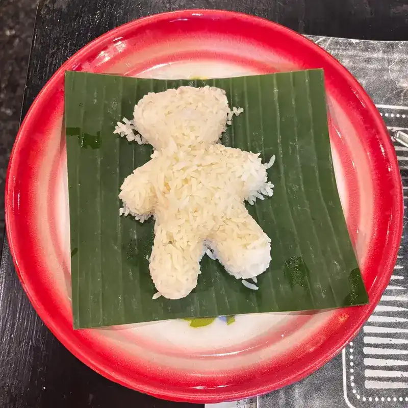 Steamed rice shaped like a little teddy bear on banana leaf, on a red-rimmed enamel plate