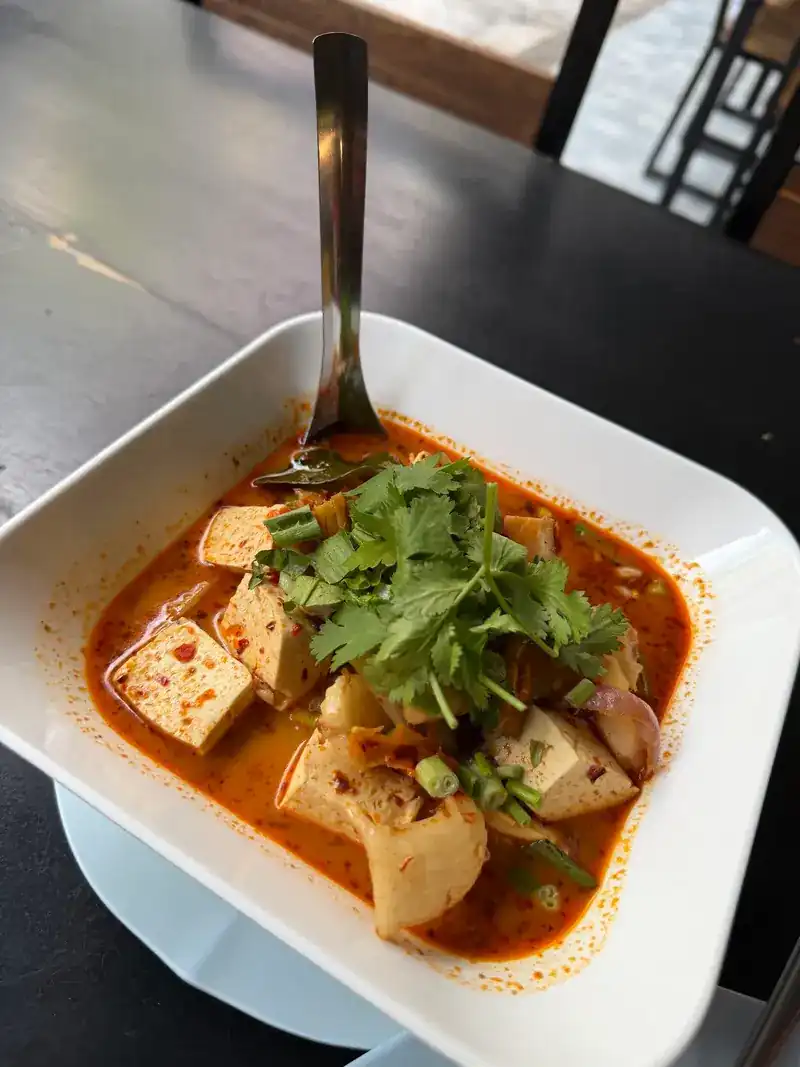 A red soup with tofu and coriander in a white bowl / ซุปน้ำสีแดงใส่เต้าหู้และผักชีในชามสีขาว