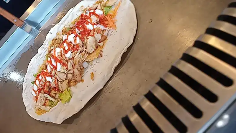 A chicken wrap being filled on the griddle, with sauces, lettuce and carrot