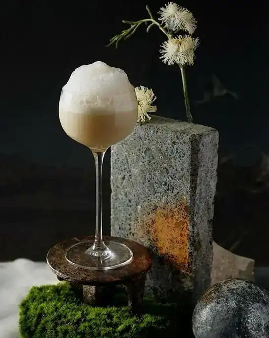 A foam-topped cocktail in a stemmed glass beside a block of grey stone