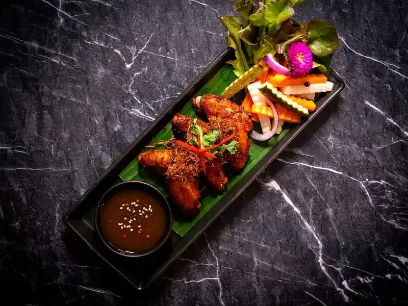 Chicken wings on banana leaf with dipping sauce and pickles