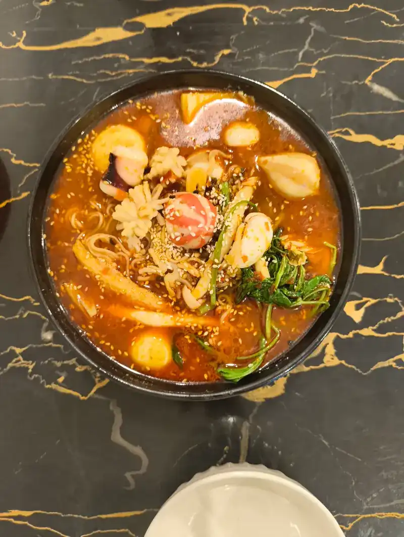 A bowl of mala soup with greens, fish balls and sesame