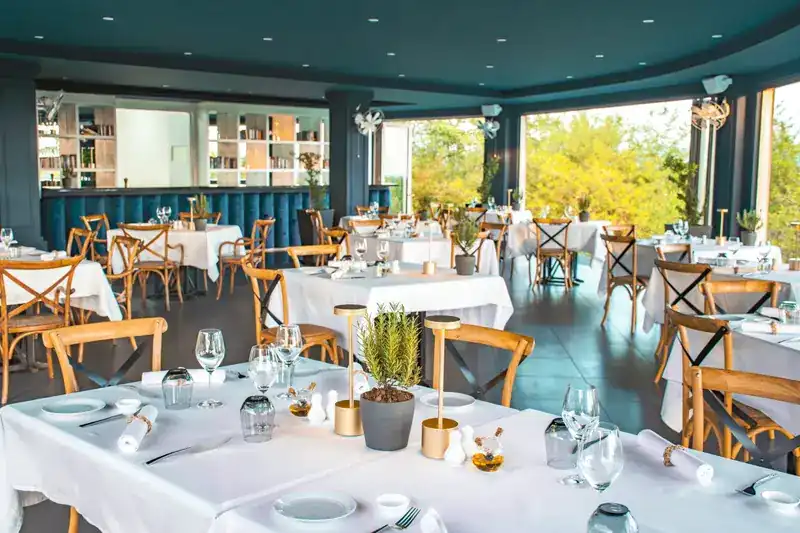 The dining room by day: white linen, oak chairs, deep teal walls and wide open windows