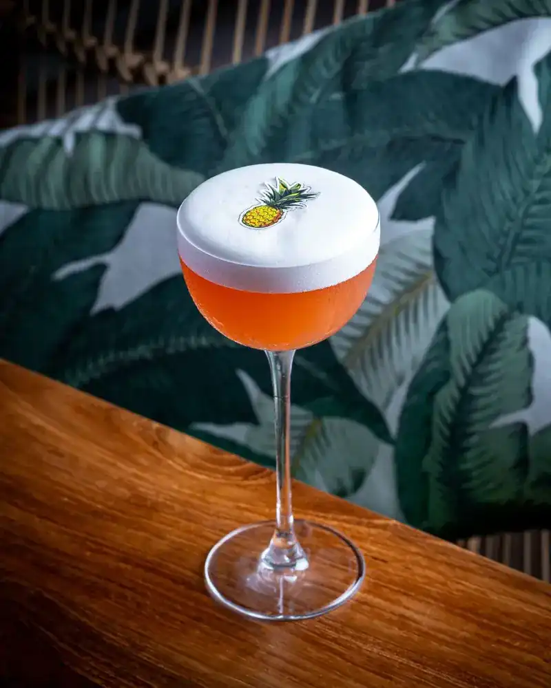 A cocktail in a stemmed glass on the wooden bar, against a banana-leaf cushion
