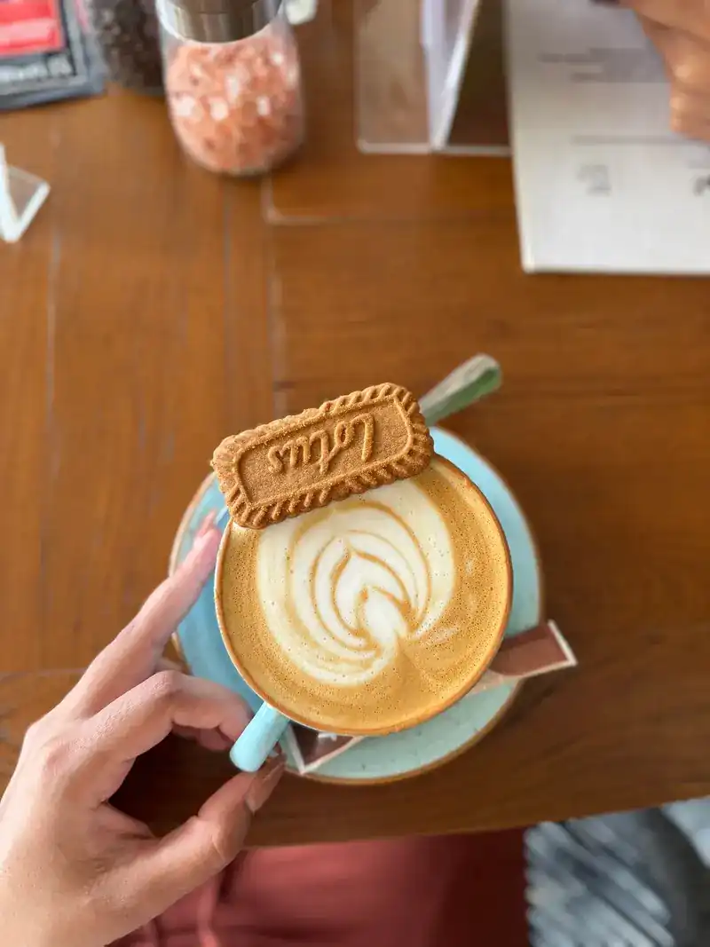 A cappuccino with a caramel biscuit on top, held in one hand over the table