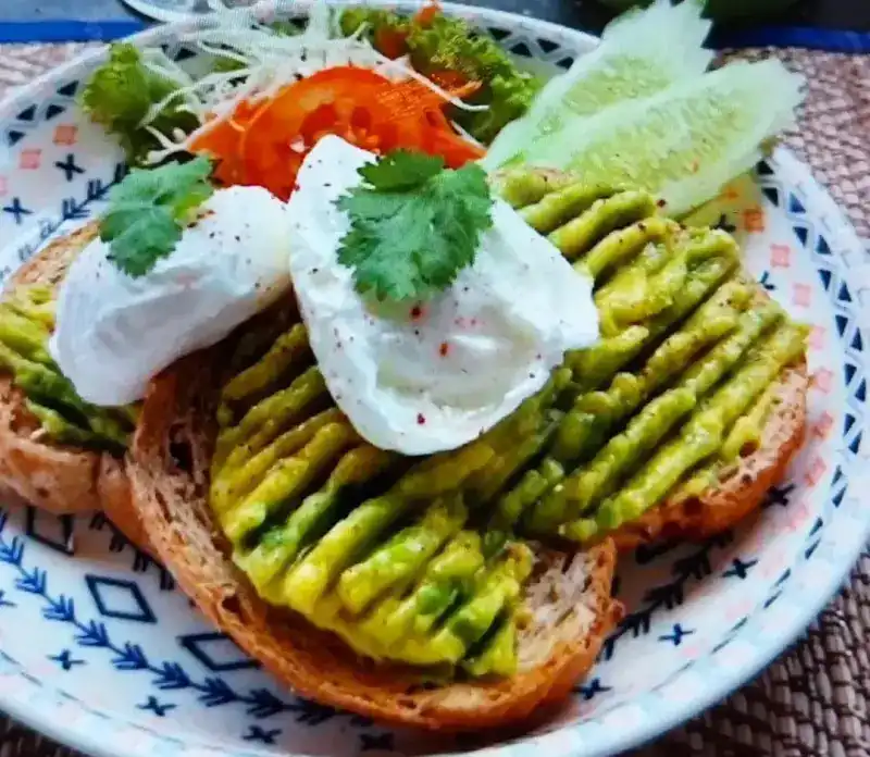 Avocado toast topped with two poached eggs and coriander, with salad on a patterned plate