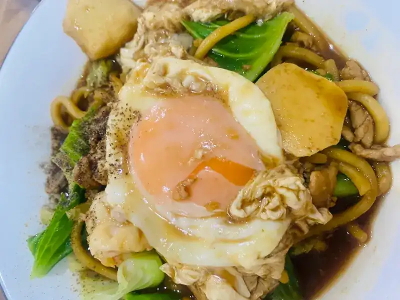 Yellow noodles in a brown sauce with a fried egg and greens